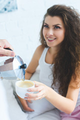 partial view of man pouring coffee to beautiful smiling woman in bedroom
