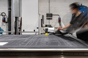 Young worker, operating a CNC machine. Big vinyl rolls ready for high quality printing. Industrial...