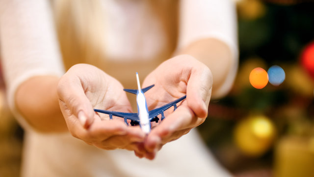 Closeup image of young woman sitting under Christmas tree and holding small toy airplane. Concept of winter holidays travelling