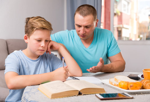Adult male is helping his son are writing homework