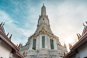 Fototapeta premium Vew of Wat Arun Buddhist temple during bright sunny day with sunset in the background, Bangkok, Thailand