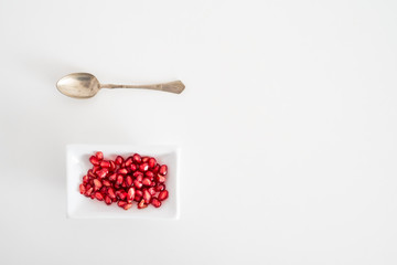 above view of pomegranate seeds in white plate and silvr teaspoon