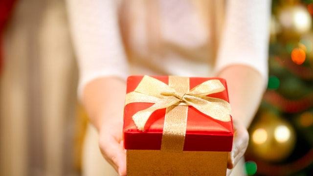Closeup image of woman in dress showing Christmas present box in camera