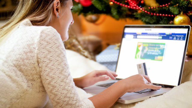 Young woman holding credit card lying on floor and ordering Christmas present online