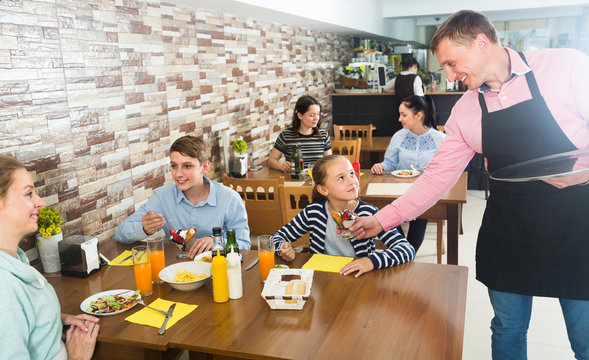 male waiter serving cheerful family in family cafe