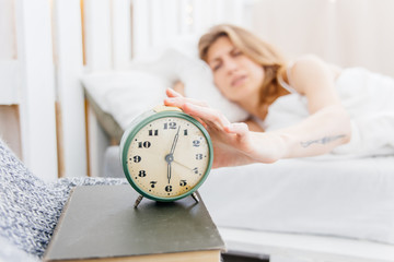 Young woman turns off the alarm clock in the morning