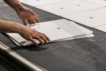 Worker, operating a cnc machine, delivering thin white boards cut into rectangular panels, ready for transport.