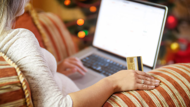 Closeup image of woman sitting next to Christmas tree and browsing online stores on laptop