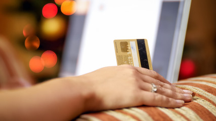 Closeup photo of young woman holding credit card browsing online stores. Christmas lights on backgorund