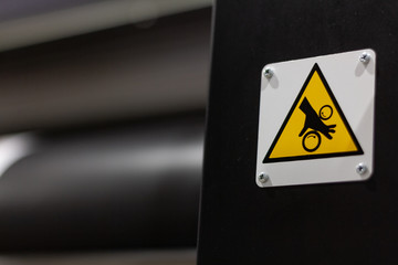 Big,  black, printers with yellow warning sign in focus and blurred rolls in background