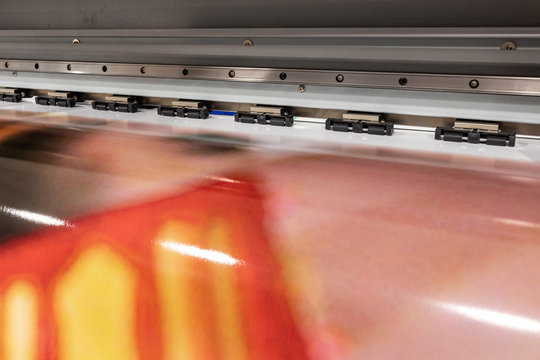 Big professional large scale printer, processing a glossy sheet of paper for color sampling. Red print on metal background.