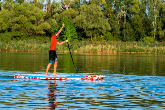 Happy guy, teenager paddling on a SUP board on large river