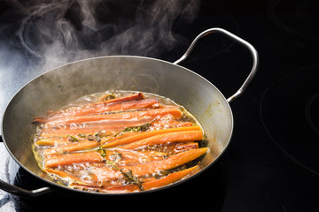 cooking carrots with herbs and spices in a steaming wok pan on the black stove, copy space