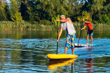 Happy friends paddling on a SUP board on large river