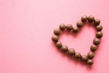 Heart shape created from chocolate balls on pink table. Love sweets. Congratulation concept. Mockup for positive idea. Empty place for inspirational, emotional, sentimental text, quote or sayings.