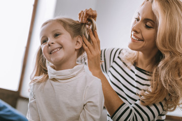 Cute hairstyle. Cheerful pleasant girl smiling while sitting in front of her mother