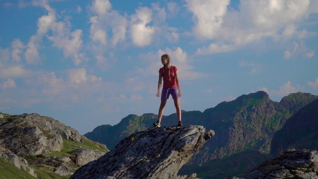 A teenage girl dances on a rock in the mountains of Norway. Crazy dancer girl having fun enjoying nature celebrating vacation travel in Lofoten island