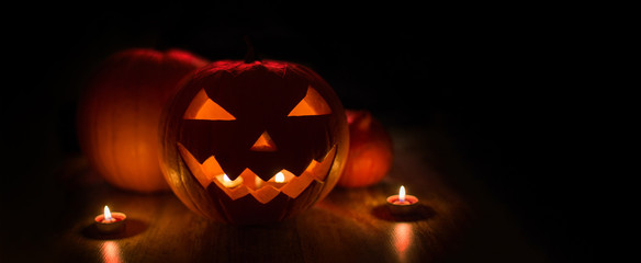 halloween and holidays concept - spooky carved pumpkin jack-o-lantern with candles in darkness