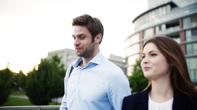 A young businessman and businesswoman walking on a bridge.