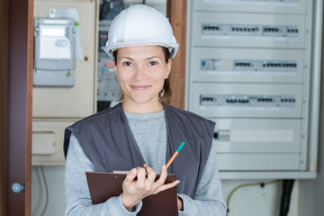 portrait of female electrician with clipboard at fusebox