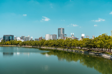 Fototapeta na wymiar OSAKA, JAPAN - AUGUST 4, 2018: Viev of Osaka city with park and river in the foreground and office buildings in the background during a bright sunny day