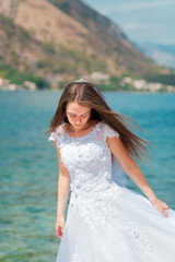 Fototapeta na wymiar Portrait of a bride in a white wedding dress on a background of the sea and mountains. Girl brown-haired with long straight hair. Young beautiful woman looking down