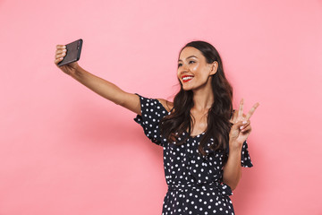 Smiling brunette woman in dress making selfie on smartphone