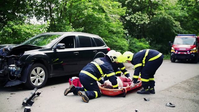 Firefighters putting an injured woman into a plastic stretcher after a car accident.