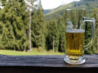 A glass of beer on a balcony rail with a forest background