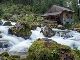Idyllic long exposure view of an old abandoned mill with rocks lying in beautiful riverbed in a mystic forest on a cloudy moody day in springtime, Golling, Salzburger Land, Austria. August, 2018 © ikmerc