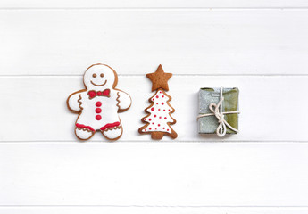Сreative Christmas composition with glazed gingerbread men, Christmas tree and gift on white wooden background, macro, flat lay. Christmas and new year concept, copy space.