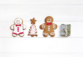 Сreative Christmas composition with white cookie and brown chocolate gingerbread men, Christmas tree and gift on white wooden background, macro, flat lay. Christmas and new year concept, copy space.