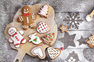 Christmas cookies of various shapes in sugar glaze on a cutting board on a brown wooden table sprinkled with flour, flat lay. Christmas composition with gingerbread men, fir-trees, rabbit.
