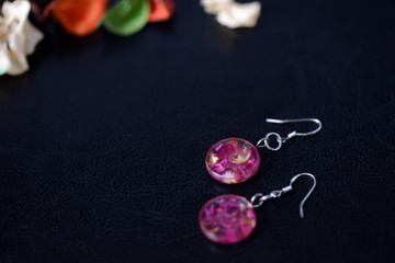 Resin earrings with dry rose petals on a dark background close up