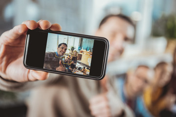 Studying process. Selective focus of male hand holding smartphone and taking selfie with colleagues