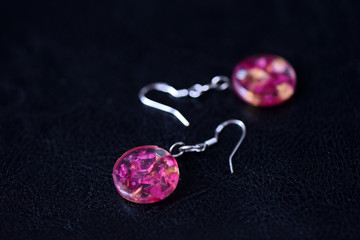 Resin earrings with dry rose petals on a dark background close up