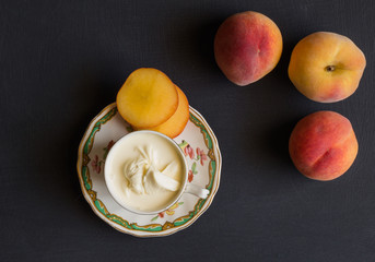 Peaches - sliced and whole and cream in a teacup on black background - Top view photo