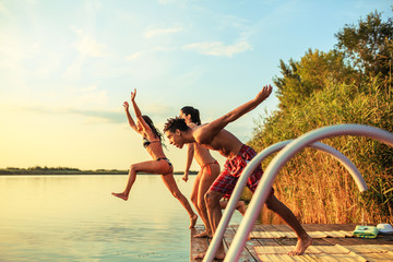 Group of friends jumping into the lake from wooden pier.Having fun on summer day.