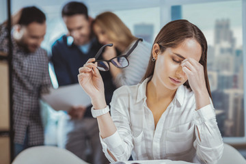 Professional burnout. Weary female colleague massaging nose bridge and holding glasses