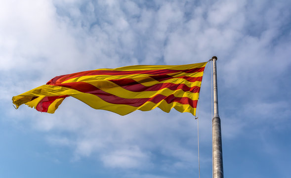 Flag of Catalonia waving in the breeze against blue sky. The flag is called The Senyera (flag in Catalan) and consists of four red stripes on yellow field. It represents the Catalan Nation and culture