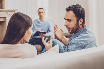 Obraz premium Family misunderstanding. Unhappy young man arguing with his wife while visiting a psychologist together