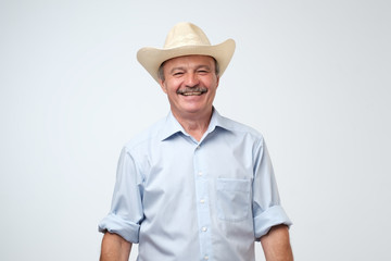 Cowboy style. Mature man adjusting his cowboy hat and laughing on joke while standing against grey...