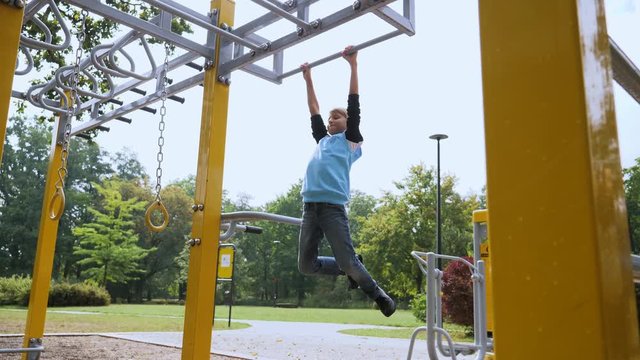 Weak frail kid boy unsuccessfully tries make pull-ups on a bar - unhealthy childhood