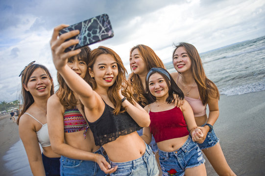 lifestyle beach portrait of Asian Korean and Chinese women, group of happy beautiful young girlfriends taking selfie picture together with mobile phone