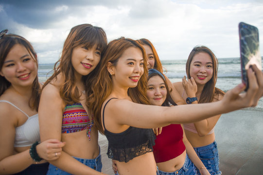 lifestyle beach portrait of Asian Korean and Chinese women, group of happy beautiful young girlfriends taking selfie picture together with mobile phone