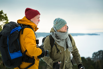 Two mature men with exploring Finland in winter. Travellers hiking and Taking pictures with camera on the top of rock. Beautiful view of northern landscape with frozen Baltic Sea and snowy islands.