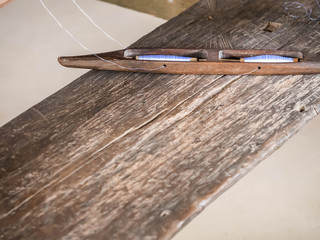 Closeup of wooden weaving boat shuttle with white cotton thread.