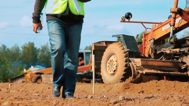 Motor grader leveling ground on construction site. Heavy machinery working in sand quarry. Close up mining industry worker going on camera. Excavation building territory for new construction