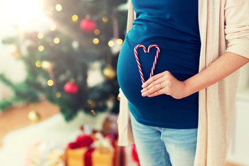 pregnancy, christmas and people concept - close up of pregnant woman with heart made of candy canes...