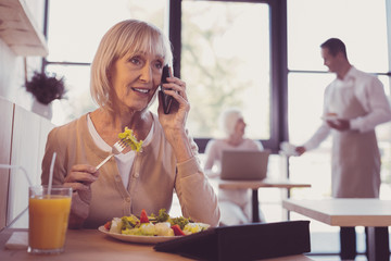 Important call. Occupied pleasant senior woman spending time in the cafe having conversation and eating.